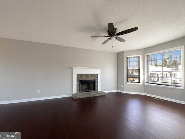 unfurnished living room with a tiled fireplace, ceiling fan, dark wood-type flooring, and a textured ceiling