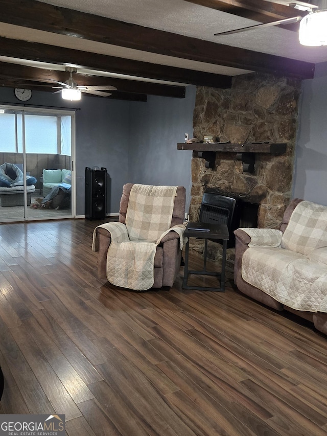 living room with ceiling fan, a stone fireplace, dark wood-type flooring, and beamed ceiling