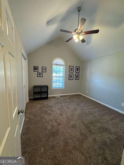 interior space with dark colored carpet, lofted ceiling, and ceiling fan