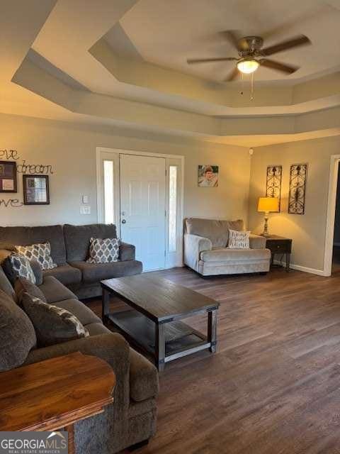 living room featuring dark hardwood / wood-style flooring, a raised ceiling, and ceiling fan