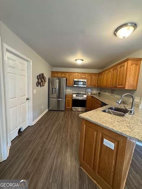 kitchen with appliances with stainless steel finishes, dark hardwood / wood-style floors, sink, kitchen peninsula, and light stone countertops