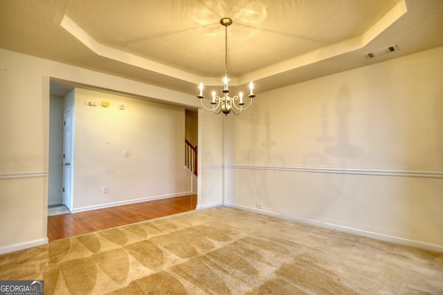 unfurnished room featuring a raised ceiling and a chandelier