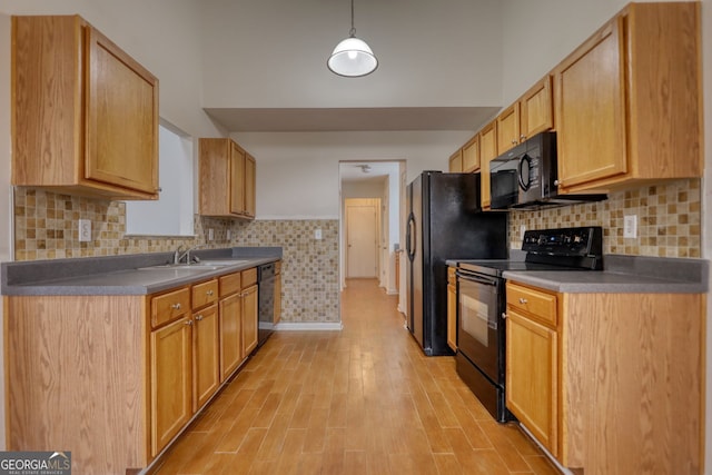 kitchen featuring sink, decorative light fixtures, light brown cabinets, light hardwood / wood-style floors, and black appliances