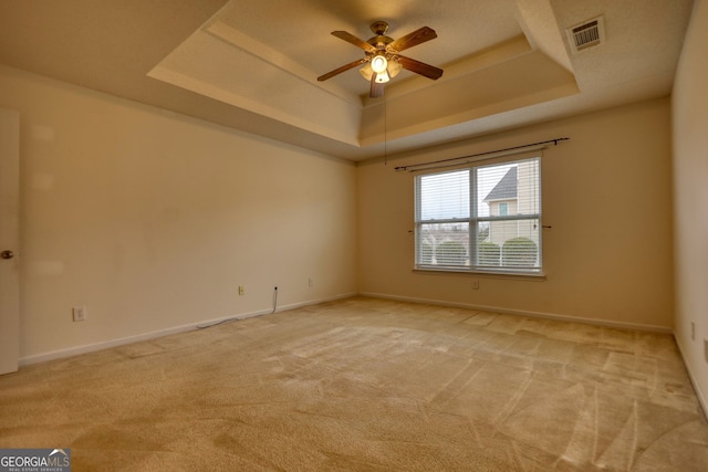 spare room with a tray ceiling, light colored carpet, and ceiling fan