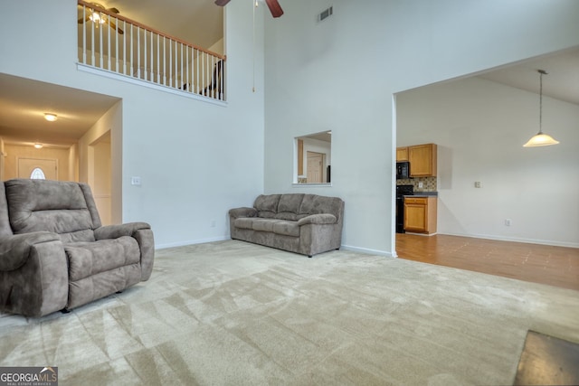 carpeted living room with ceiling fan and a high ceiling