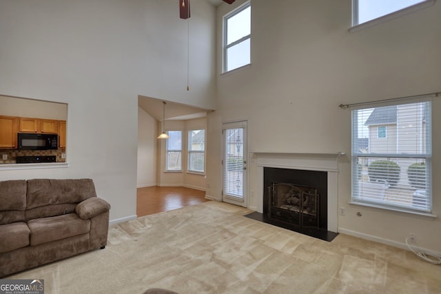 carpeted living room featuring ceiling fan, a wealth of natural light, and a high ceiling