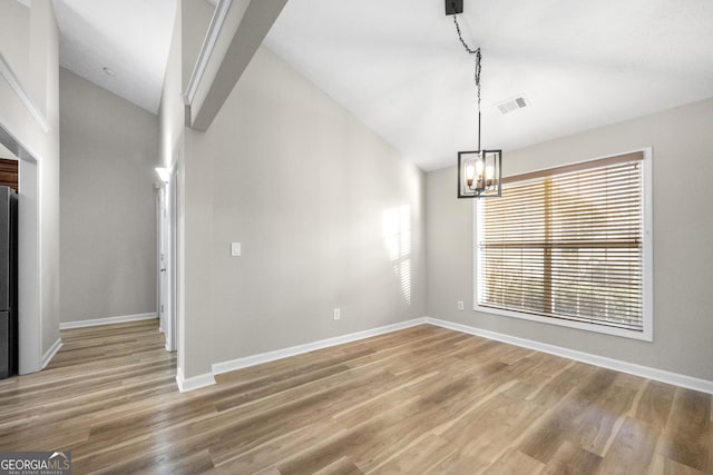 unfurnished dining area featuring light wood finished floors, baseboards, visible vents, and vaulted ceiling