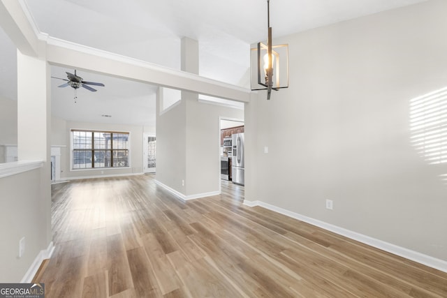 unfurnished living room with light wood-style flooring, baseboards, vaulted ceiling, and ceiling fan with notable chandelier