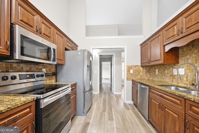 kitchen with light stone counters, stainless steel appliances, a towering ceiling, a sink, and light wood-type flooring