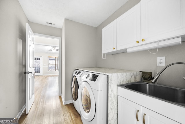 clothes washing area featuring sink, washing machine and dryer, cabinets, light hardwood / wood-style floors, and a textured ceiling