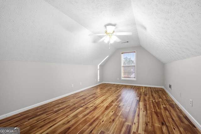 additional living space with ceiling fan, wood-type flooring, a textured ceiling, and vaulted ceiling