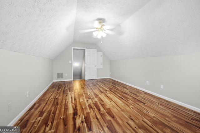 additional living space with lofted ceiling, hardwood / wood-style floors, a textured ceiling, and ceiling fan