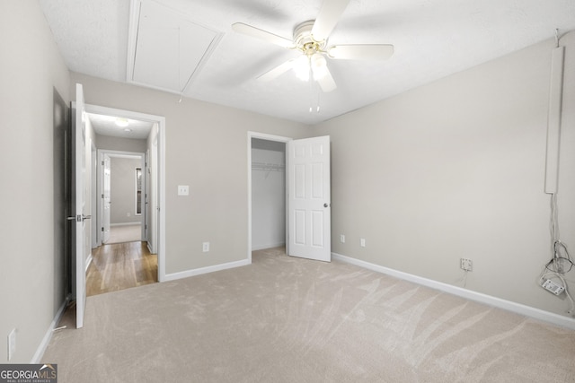 unfurnished bedroom featuring light carpet, a ceiling fan, baseboards, a closet, and attic access