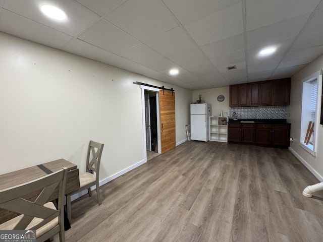 interior space with baseboards, visible vents, a barn door, a drop ceiling, and light wood finished floors