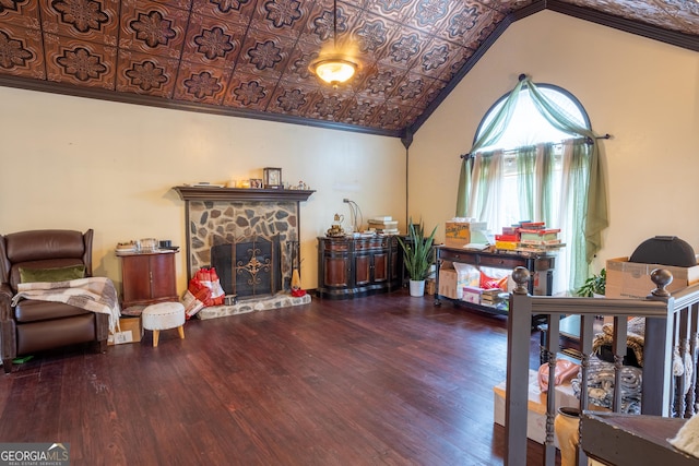 living area with ornamental molding, an ornate ceiling, a stone fireplace, lofted ceiling, and wood finished floors