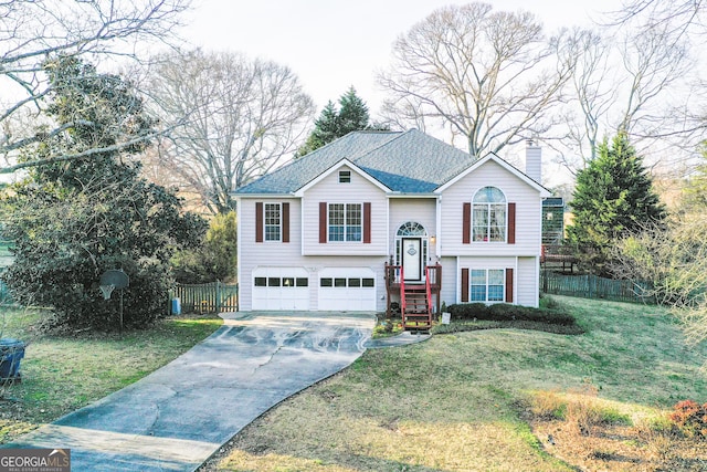 raised ranch featuring fence, a chimney, a garage, concrete driveway, and a front lawn