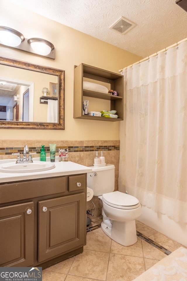 bathroom with a wainscoted wall, tile walls, visible vents, a textured ceiling, and toilet