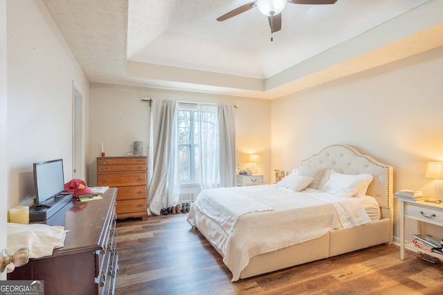 bedroom featuring dark wood finished floors, ceiling fan, and a raised ceiling