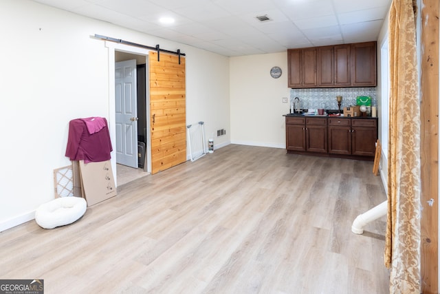 bar featuring baseboards, light wood finished floors, visible vents, and a barn door