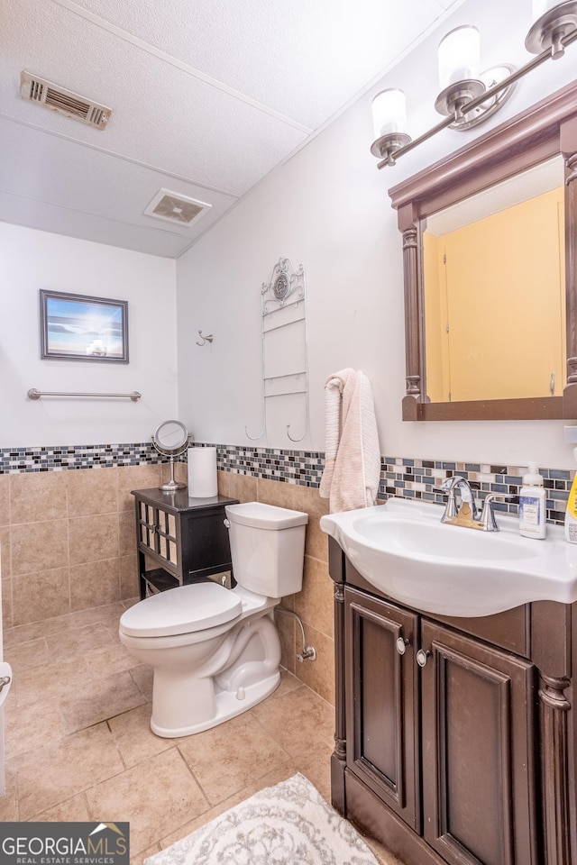 bathroom with vanity, tile walls, visible vents, toilet, and tile patterned floors