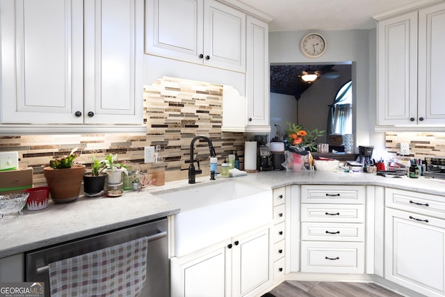 kitchen featuring stainless steel dishwasher, a sink, white cabinetry, light stone counters, and backsplash