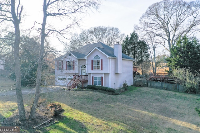 bi-level home with an attached garage, a chimney, a front yard, and fence