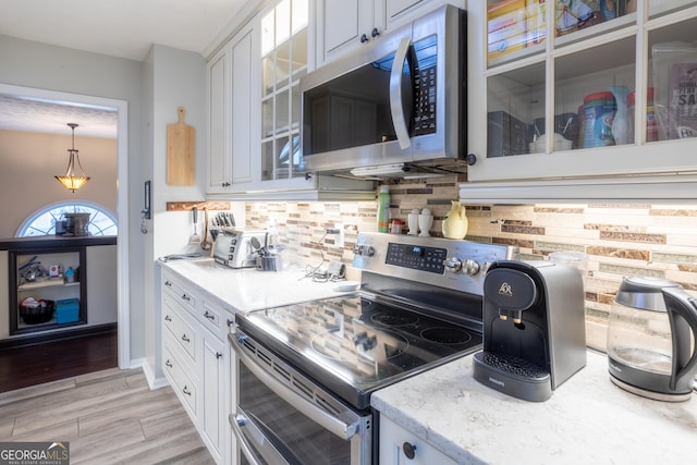 kitchen featuring glass insert cabinets, white cabinetry, light stone countertops, backsplash, and appliances with stainless steel finishes