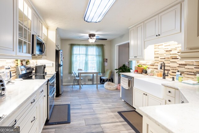 kitchen featuring decorative backsplash, glass insert cabinets, white cabinetry, a ceiling fan, and appliances with stainless steel finishes