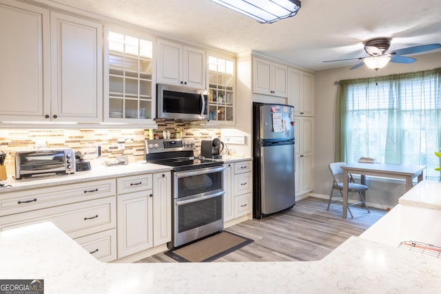 kitchen featuring stainless steel appliances, light countertops, tasteful backsplash, and glass insert cabinets