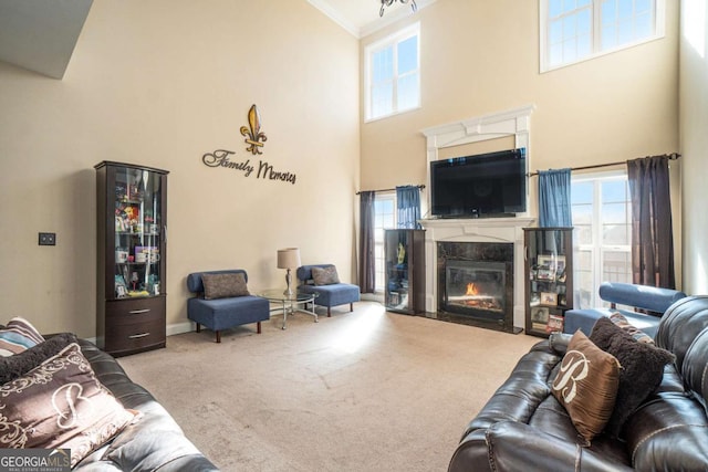 living area featuring carpet floors, ornamental molding, a high ceiling, and a high end fireplace