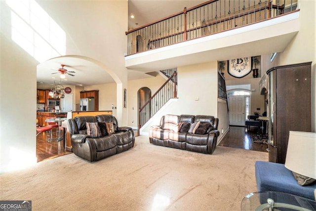 living area featuring carpet, arched walkways, stairway, a towering ceiling, and a ceiling fan