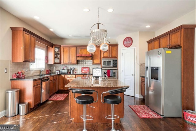 kitchen featuring brown cabinetry, a kitchen island, appliances with stainless steel finishes, a breakfast bar, and backsplash