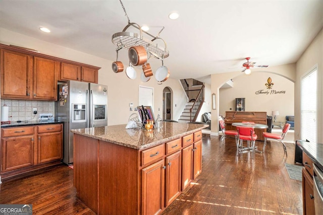 kitchen with arched walkways, tasteful backsplash, brown cabinetry, and stainless steel fridge