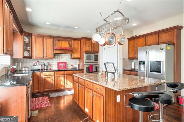 kitchen featuring dark wood finished floors, dark stone counters, custom range hood, stainless steel appliances, and a sink