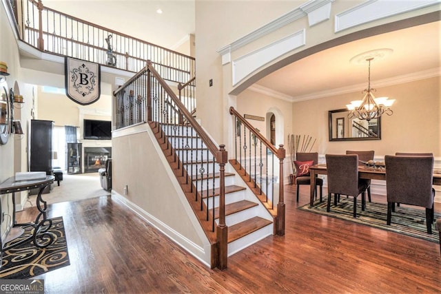 staircase featuring arched walkways, a glass covered fireplace, wood finished floors, and crown molding