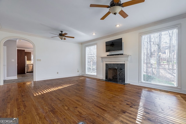 unfurnished living room featuring dark hardwood / wood-style flooring, ornamental molding, ceiling fan, and a high end fireplace