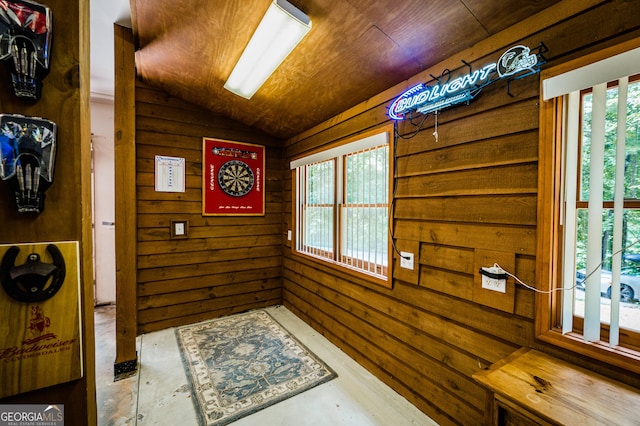 doorway with wooden walls, concrete flooring, vaulted ceiling, and wooden ceiling