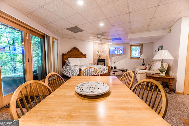 dining room featuring ceiling fan, plenty of natural light, a stone fireplace, and a paneled ceiling