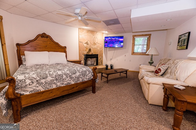 bedroom featuring ceiling fan, carpet flooring, a fireplace, and a drop ceiling