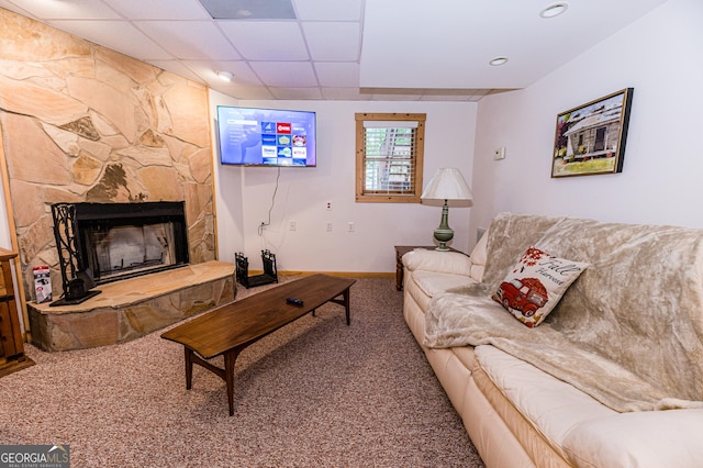 carpeted living room with a stone fireplace and a drop ceiling