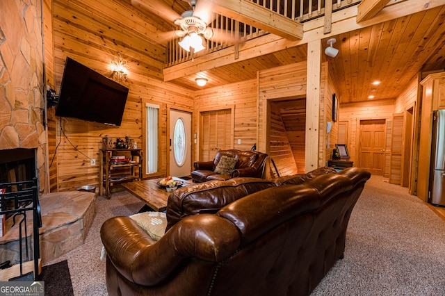 carpeted living room featuring a stone fireplace, wooden ceiling, wooden walls, ceiling fan, and a high ceiling