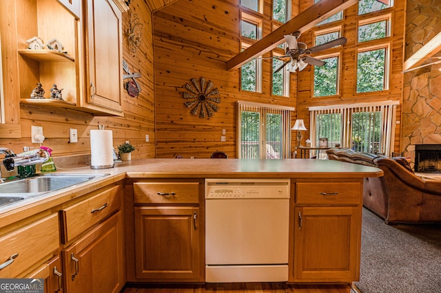 kitchen featuring a stone fireplace, wood walls, dark carpet, kitchen peninsula, and white dishwasher