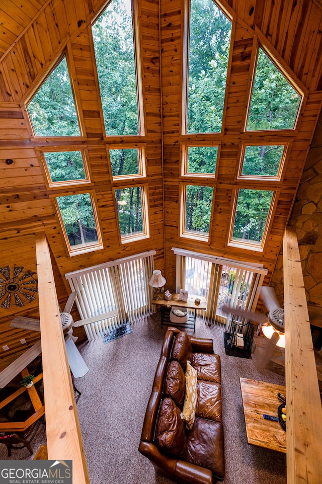 living room with carpet floors, high vaulted ceiling, wooden walls, and plenty of natural light