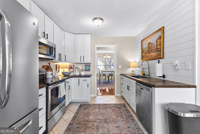 kitchen featuring appliances with stainless steel finishes, white cabinetry, sink, light tile patterned floors, and a textured ceiling