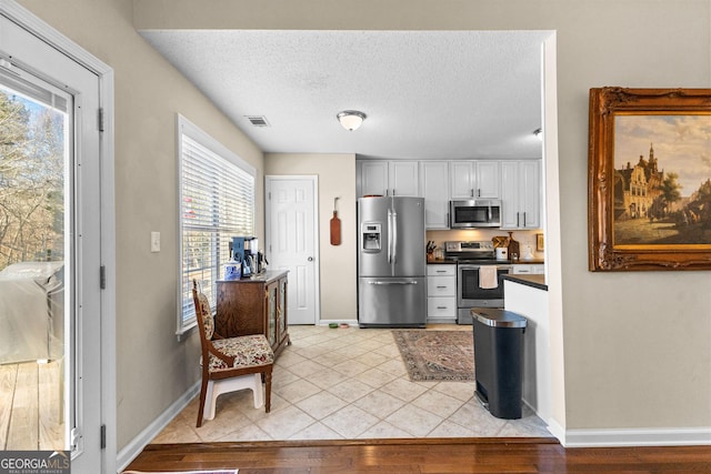 kitchen with light tile patterned floors, a textured ceiling, white cabinets, and appliances with stainless steel finishes