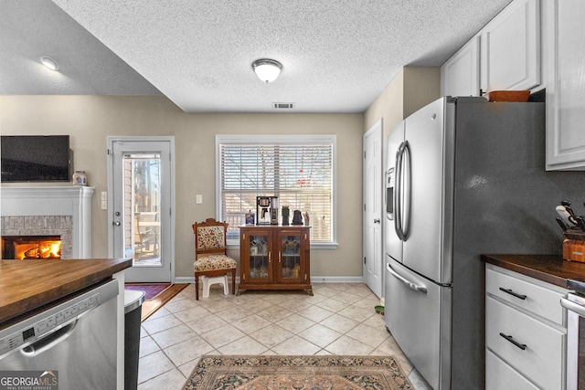 kitchen featuring appliances with stainless steel finishes, a fireplace, white cabinets, light tile patterned floors, and a textured ceiling