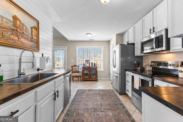 kitchen with appliances with stainless steel finishes, wood counters, white cabinetry, sink, and a textured ceiling