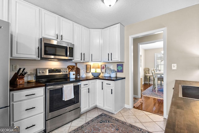 kitchen featuring white cabinetry, stainless steel appliances, light tile patterned flooring, and a textured ceiling