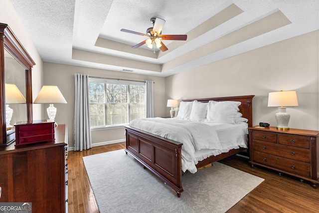 bedroom featuring dark wood-type flooring, ceiling fan, a raised ceiling, and a textured ceiling