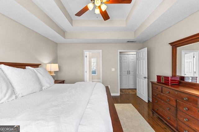 bedroom featuring dark wood-type flooring, ceiling fan, a raised ceiling, and ensuite bath